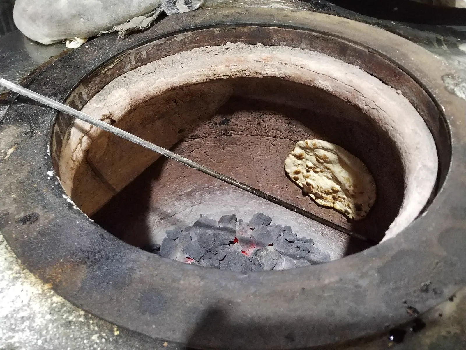 A roti baking inside a clay tandoor over hot coals